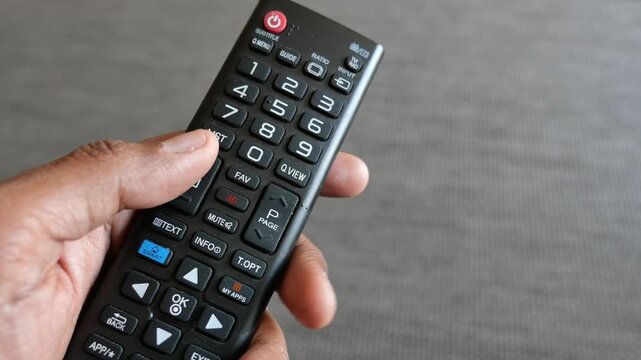 Close up view of a man pressing the volume up button on an LG smart TV remote control, changing channels with a focus on technological interaction