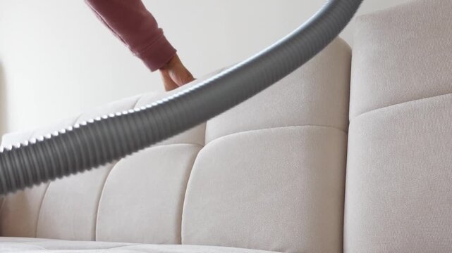 Close up video of person cleaning white sofa backrest with vacuum cleaner, showing meticulous home maintenance and cleanliness