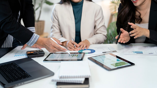 Professional business team collaborating and analyzing financial reports on digital tablets and documents at a modern office desk.