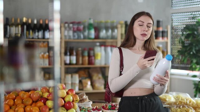 Female buyer checks suitability - scans QR code on bottle of milk label in a grocery store. High quality 4k footage
