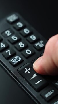 Vertical macro shot of a hand pressing the mute button on a TV remote, showing audio control and quick sound toggling in a modern home entertainment setup.