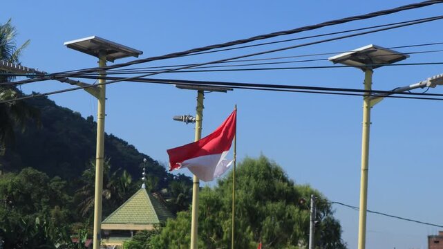 Video of the Indonesian flag, Red and White, flying on a pole among lights against a blue sky background.