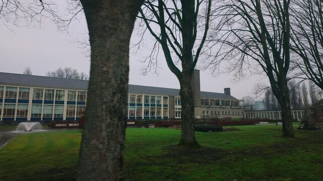 Wide shot of SGA educational facility in Arnhem Netherlands with bare trees and fountain in front, showcasing the modernist facade and surrounding green space in winter.