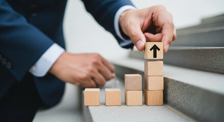 Businessman in blue suit building wooden block staircase with upward arrow symbolizing growth and success on gray steps