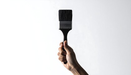 A hand holds a black-bristled paintbrush against a bright white backdrop, showcasing its details and simple form
