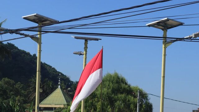 Video of the Indonesian flag, Red and White, flying on a pole among lights against a blue sky background.