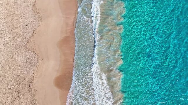 A sandy sea beach background with turquoise sea waves. Looping ocean texture, aerial view of calmly moving ocean waves. Flying over a sandy beach and waves, seamless beach loop.