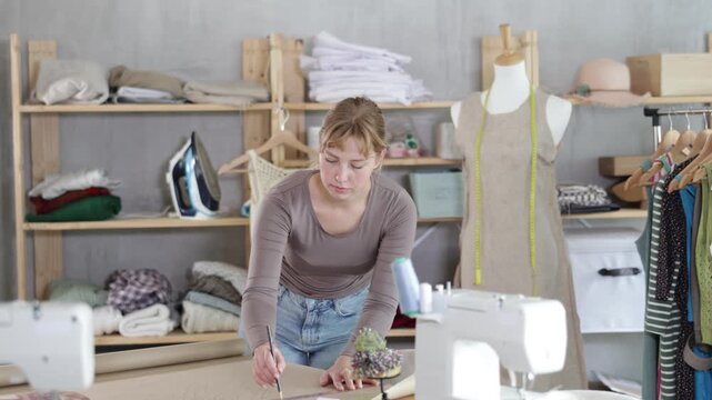 Female fashion designer drafting clothing pattern on paper in studio 