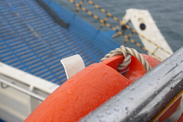 Wet Metal Handrail and Orange Lifebuoy on Ship Deck with Raindrops