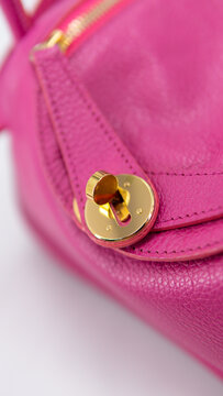Macro detail of a golden twist lock closure on a vibrant pink leather handbag