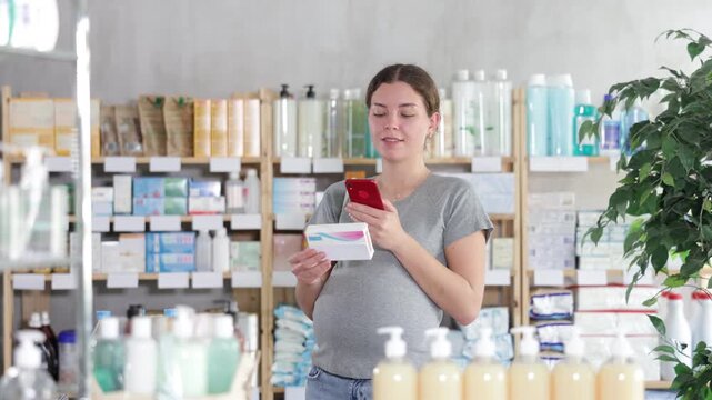 Positive pregnant woman choosing box with pills to improve well-being in modern pharmacy, scan QR code on label