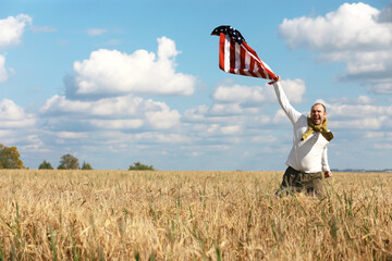 Fototapeta premium Man waving American flag standing in grass farm agricultural field , holidays, patriotism, pride, freedom, political parties, immigrant