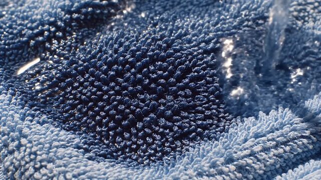 Macro Close Up Of Blue Towel Fabric Fibers Absorbing Water Creating Dark Damp Patch With Soft Lighting