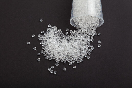 Virgin GPPS pellets, close-up. Virgin polystyrene granules spilled out of plastic container into dark table. Granulated plastic polymer. PS granules or EPS beads