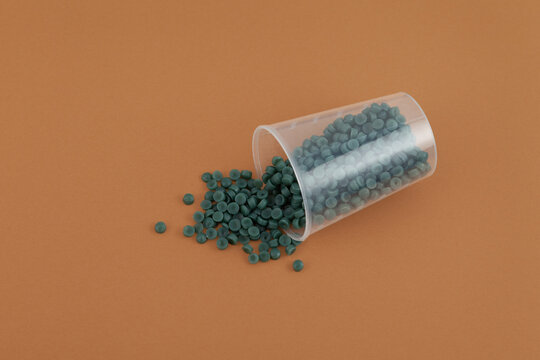 Recycled polypropylene granules rPE spilled out of plastic cup on brown. Secondary polypropylene. Granulated plastic polymer for production of plastic products