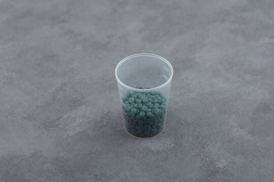 Recycled Polypropylene or rPP granules in disposable plastic cup on grey background. Reprocessed Polypropylene (post-industrial). Secondary plastic polymer