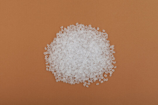 Heap of Virgin polypropylene pellets or virgin PP granules on brown background, top view. Granulated plastic polymer. Prime PP. Base polymer for production of plastic packaging
