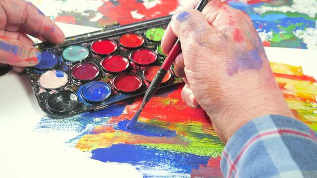 The hands of the artist, work to create creative images in art. Art paints and brushes, applying multi-coloured strokes to the canvas using palette, gouache and watercolour.
