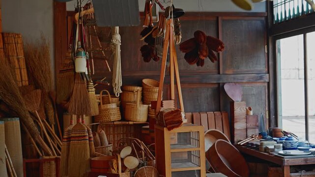 A detailed view of various handcrafted household items at Edo-Tokyo Open Air Architectural Museum. Features bamboo baskets, straw brooms, and woven sieves used in old Japanese daily life.
