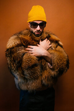 Stylish man wearing a yellow beanie, sunglasses, and fur coat