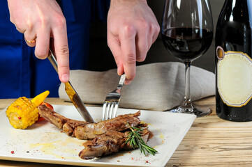 Man cutting grilled meat with knife and fork at dinner