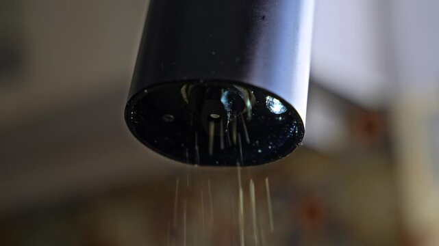 Closeup view of electric pepper grinder milling black pepper. Kitchen appliance crushing spice with rotating mechanism during cooking.