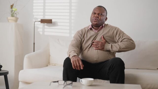 Mature african american man feeling ache when sitting at home, heart attack. Aging and disease of old age, symptom of myocardial infarction, emergency medical help, modern healthcare for aged people