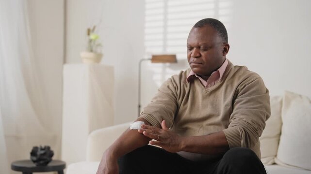 African american male person applying transdermal patch with medicine for curing chronic disease. Portrait of mature sick man in apartment, modern treatments for curing nicotine addiction, healthcare