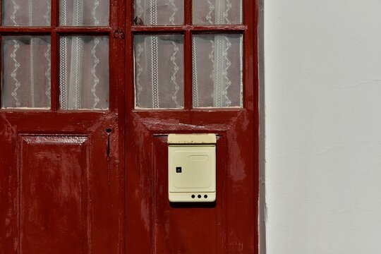 Antique wine red wooden door with handmade lace curtains and a faded metal mailbox on a whitewashed wall in Leonidio, Arcadia Peloponnese, Greece.