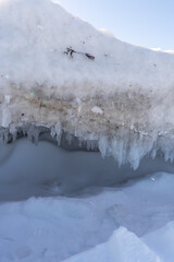Abstract winter texture with small ice cave, translucent icicles and dense snow creating sculptural frozen landscape patterns.