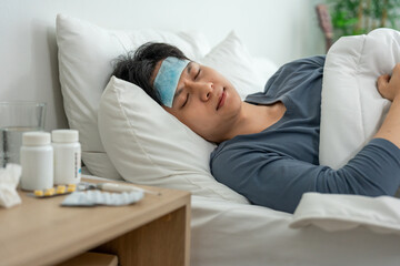 Fototapeta premium Asian young man lying down on bed in bedroom, looking sick and unwell. 
