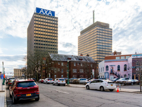 Syracuse, NY - Jan 14, 2020: Downtown Syracuse streetscape with AXA Towers and the historic State Tower Building rising behind low‑rise brick storefronts, parked vehicles, and winter trees in a mixed‑