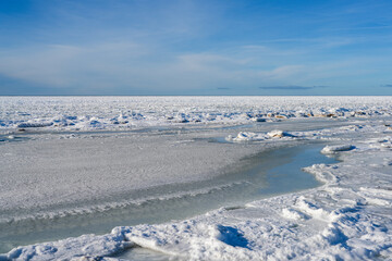 Frozen Baltic Sea Shoreline with Ice Floes and Snow Under Clear Winter Sky © Zigmunds