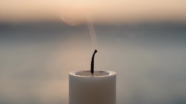 A close-up of a snuffed candle with wisps of smoke rising against a softly lit background