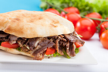 Traditional Turkish Meat Doner Kebab Served in Gobit Pita Bread with Fresh Lettuce and Tomatoes on a White Plate