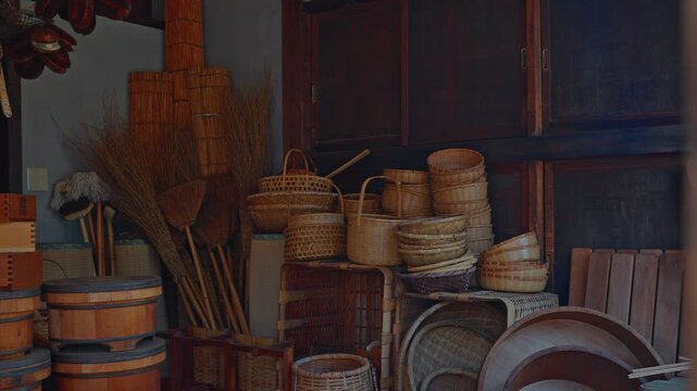 A cinematic shot of stacked traditional Japanese bamboo ware. Features various sizes of handcrafted baskets and sieves in a rustic, historic interior at Edo-Tokyo Open Air Architectural Museum.