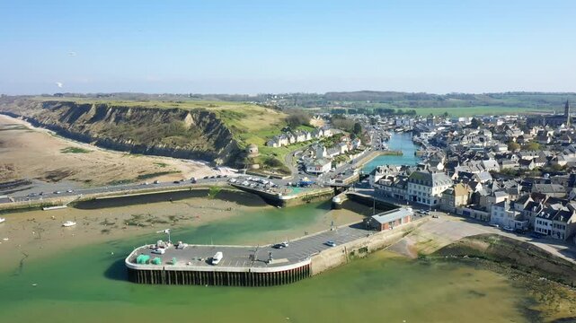 Scenic aerial view of Port en Bessin harbor with coastal cliffs, traditional houses, and calm waters under a clear blue sky in Normandy, France.