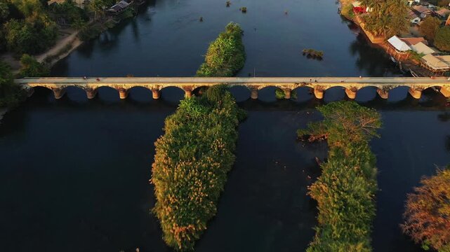 Aerial view of the historic French colonial bridge spanning a river between Don Det and Don Khon islands in Laos, surrounded by lush vegetation and village houses.