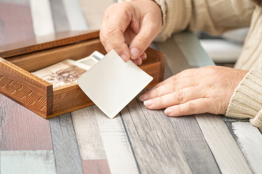 Mockup Vintage empty photographs in female hand, brown wooden box, Tracing family roots through images, journey into ancestry, family history and heritage, nostalgia template, antique artwork