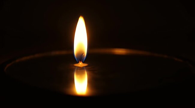 A single flame burns brightly with a reflected glow on a dark surface