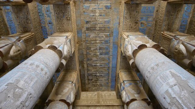Looking up inside ancient Hathor Temple at Dendera, Egypt. Painted blue ceiling with gods and hieroglyphs between massive stone columns. Rare authentic temple footage. Downscaled from 6k.
