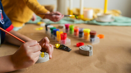 Children's hands painting small objects with colorful paints on a craft table