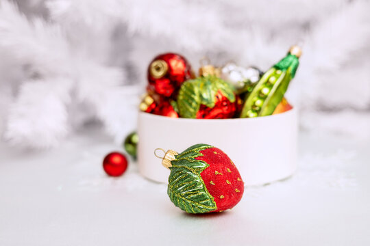 A set of multicolored glass Christmas tree ornaments in a round box against a white Christmas tree background. Single-color New Year's decor. 