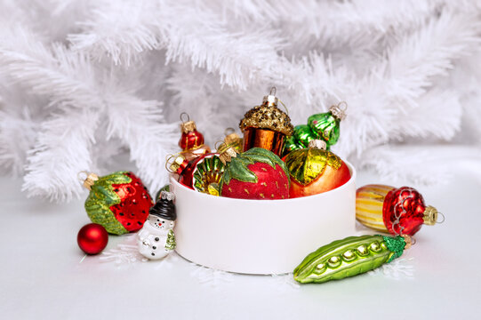 A set of multicolored glass Christmas tree ornaments in a round box against a white Christmas tree background. Single-color New Year's decor. 