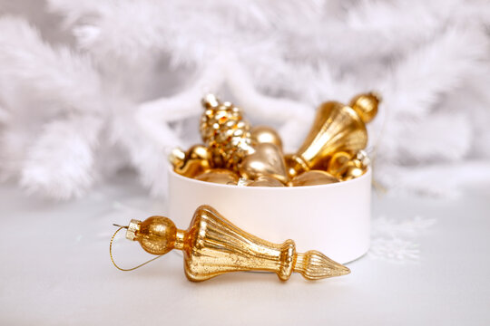 A set of gold glass Christmas tree ornaments in a round box against a white Christmas tree background. Single-color New Year's decor. 