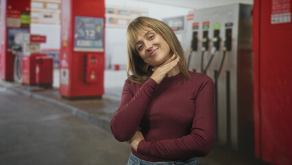 Woman touching her neck with hand at gas station, smiling with a head tilt and crossed arm pose near fuel pump  contentment. © Krakenimages.com