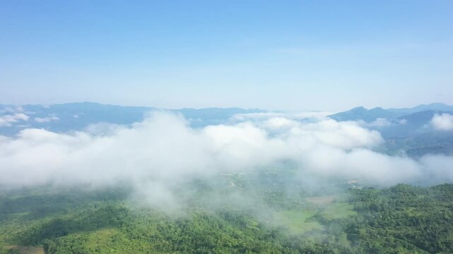 Aerial view of lush green mountains and valley in Dien Bien Phu, Vietnam, with low clouds drifting above the landscape under a clear blue sky.