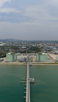 Aerial view of the Map Ta Phut LNG terminal stretching out into the sea with large green storage tanks gleaming under the sky, Map Ta Phut, Rayong, Thailand.