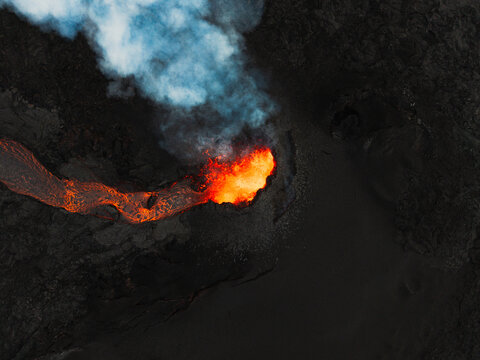 Aerial view of fiery lava flowing like molten gold against the stark, dark earth, contrasting with the ethereal smoke rising above, Grindavik, Iceland.