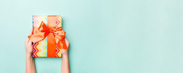Obraz premium Woman hands give wrapped christmas or other holiday handmade present in colored paper. Present box, decoration of gift on Blue table, top view with copy space